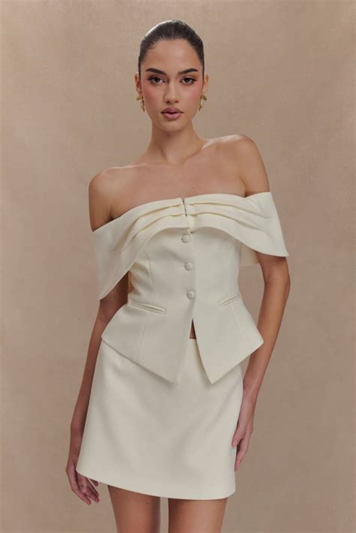model wears an ivory mini dress with trailing cape